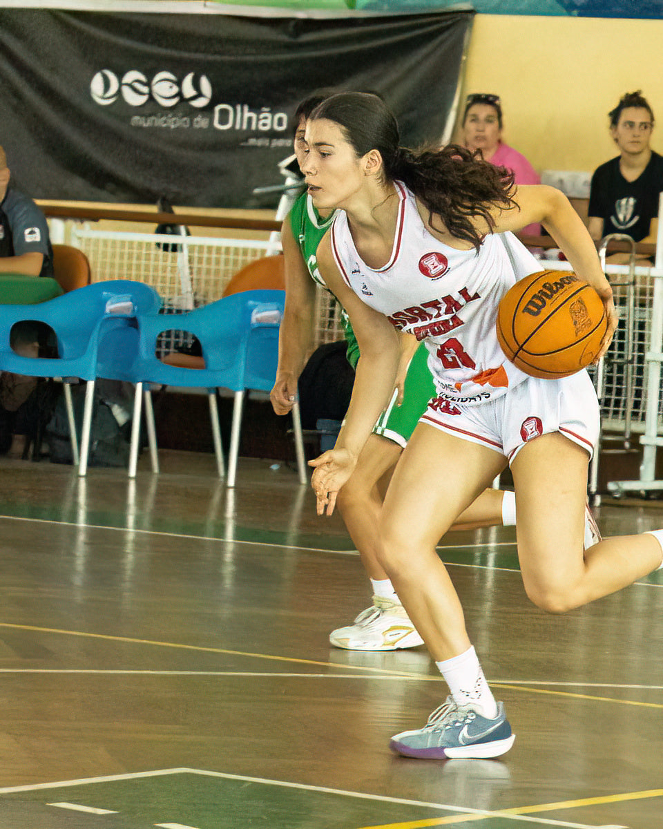 Basketball player in action on a court with a visible brand logo in the background.