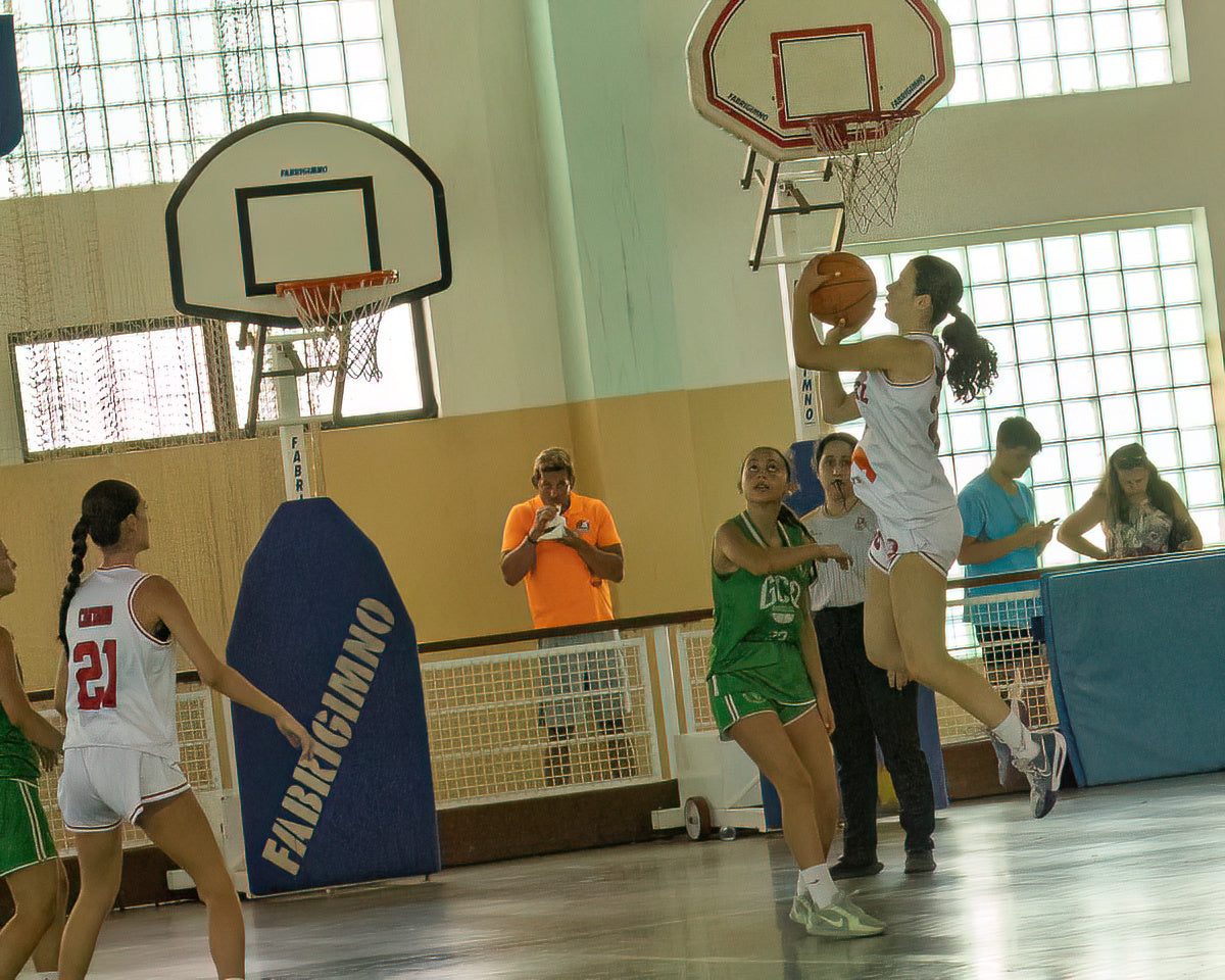Basketball game in progress with players and a referee in an indoor court.