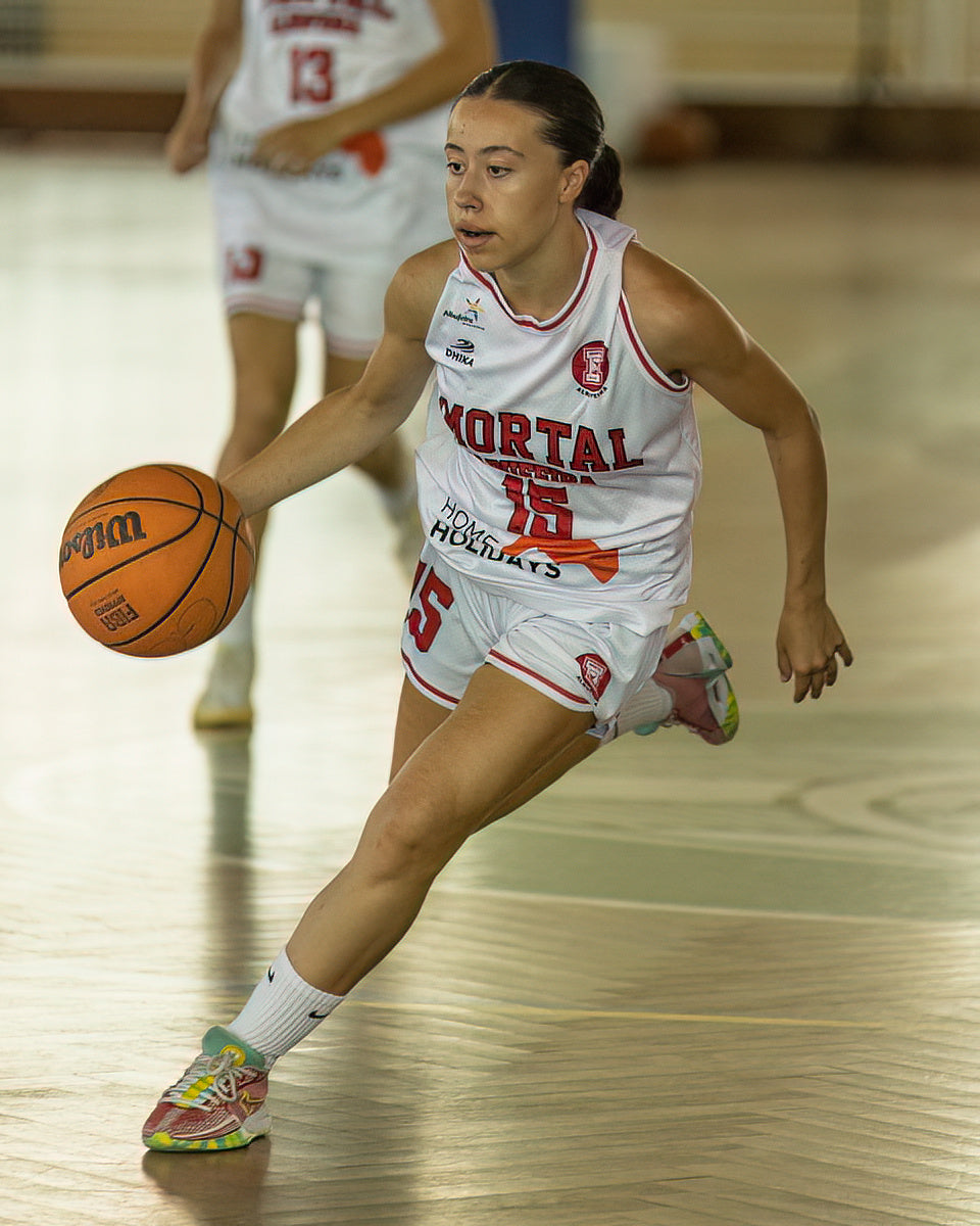 Woman playing basketball on a court with 'Mortal' branding