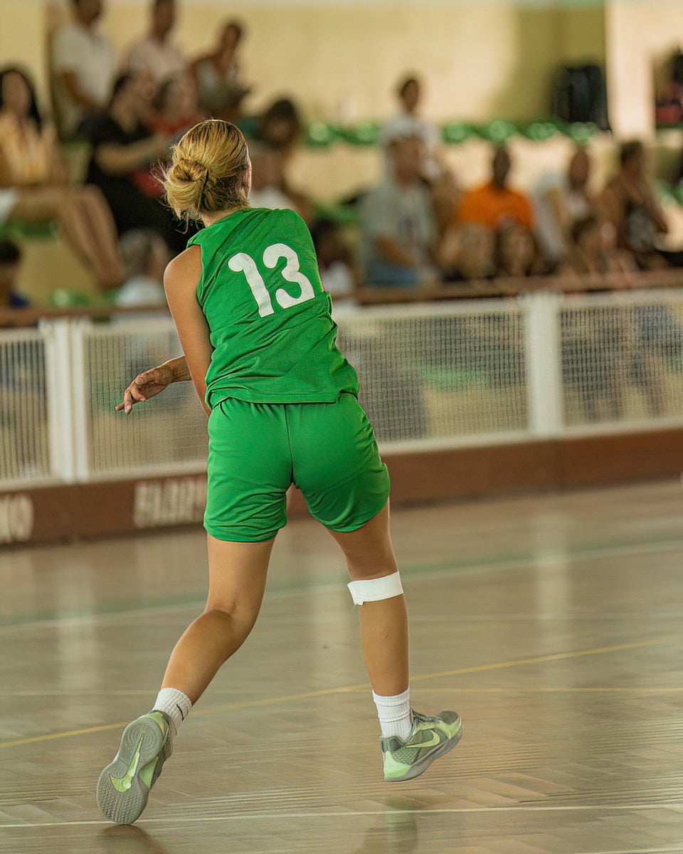 Person in a green sports uniform with number 13 on an indoor court.