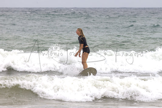 A woman in a black swimsuit stands in foamy ocean waves under an overcast sky, with a large 'Antonio Jose Sargadelos Photography' watermark across the center.