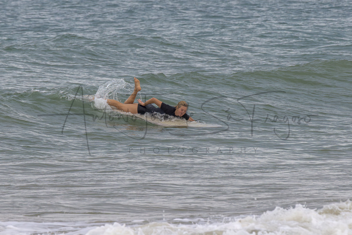 A surfer in a black swimsuit lies on a surfboard on a small ocean wave, with a large black photographer's watermark across the center reading 'Antonio Jose de la Fragoso Photography'.
