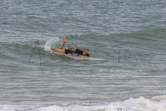 A surfer in a black swimsuit lies on a surfboard on a small ocean wave, with a large black photographer's watermark across the center reading 'Antonio Jose de la Fragoso Photography'.