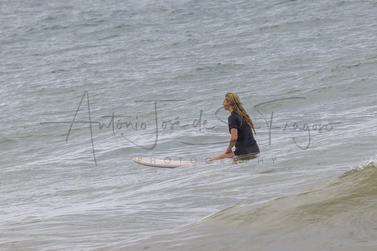 A surfer wearing a black wetsuit sits on a white surfboard in the ocean water, facing away from the camera. A large cursive watermark reading 'Antonio José de la Fuente Photography' is overlaid across the center.