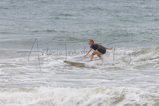 A woman in a dark gray t-shirt and black shorts surfing on a wave, with a large watermark reading 'Antonio Jose de Sruiga Photography' across the center.