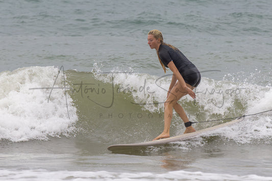 A woman in a black wetsuit stands on a surfboard in the ocean, riding a breaking wave. A large black script watermark reading 'Antonio José de Ságuro Photography' is overlaid across the center.
