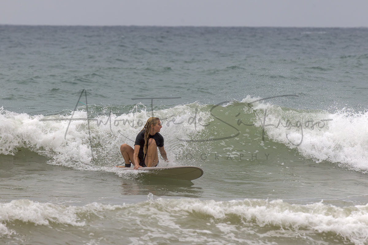 A surfer in a black wetsuit sits on a surfboard on a small ocean wave, with the photographer's watermark 'Antonio José de Sá Fragoso Photography' across the center.