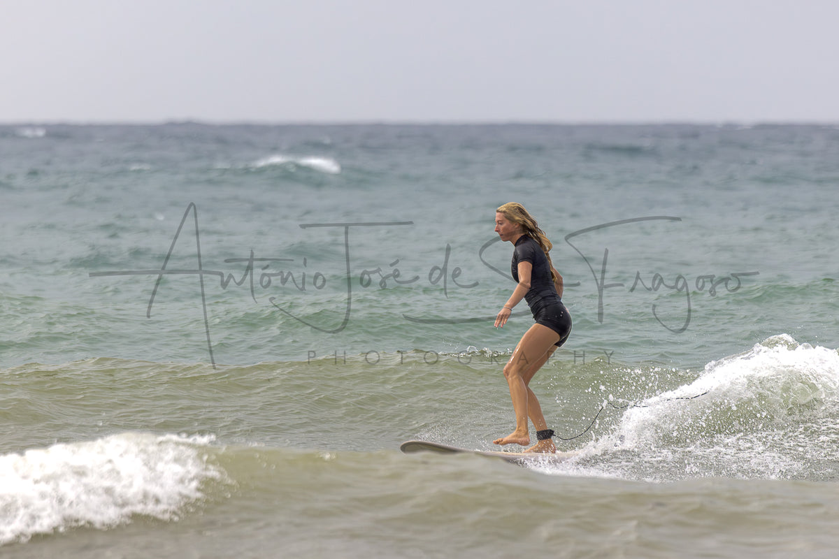 A woman in a black wetsuit stands on a surfboard in the ocean, with waves around her and a large photographer watermark reading 'Antonio José de Fragoso Photography' across the center.