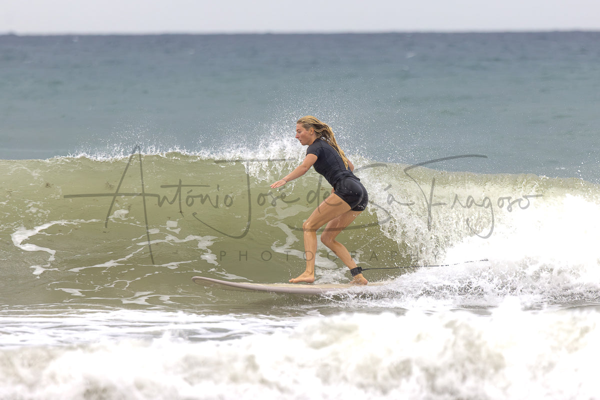 A woman in a black swimsuit surfing on a wave in the ocean, with a large photographer's watermark across the center.
