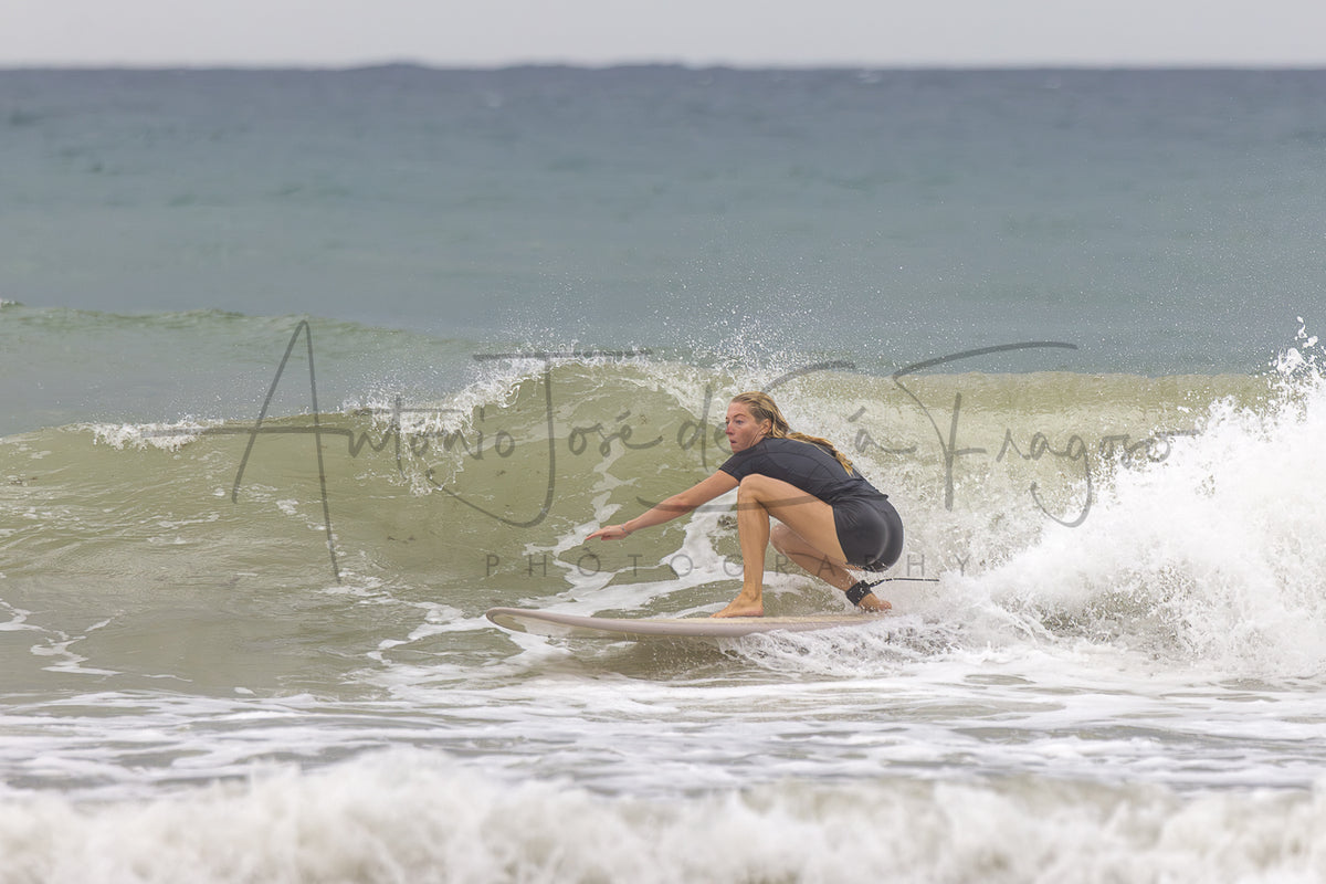 A surfer rides a breaking ocean wave, wearing a dark wetsuit, with large overlaid script text reading 'Antonio José de Sá Fragoso' and 'Photography' across the center. The scene is an outdoor beach/ocean environment with white surf, blue-gray water, and a pale sky.