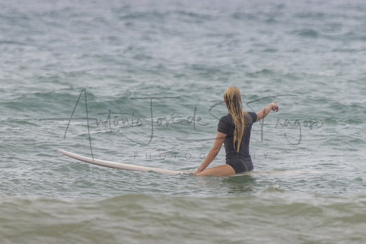 A woman in a dark gray swimsuit sits on a white surfboard in the ocean, viewed from behind. A large black script watermark reading 'Antônio José de Souza Photography' is overlaid across the center.