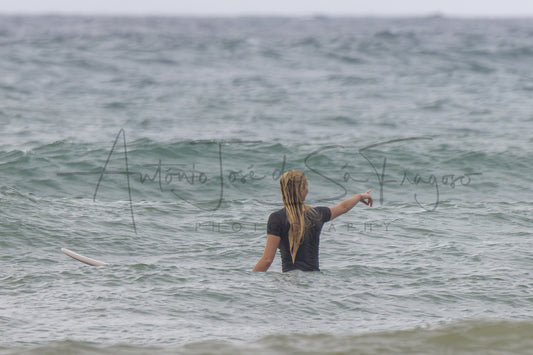 A woman stands in ocean water facing the sea, with a surfboard visible at the left edge. A large black script watermark reading 'Antonio José de Sá Fragoso' and smaller 'PHOTOGRAPHY' text is overlaid across the center.