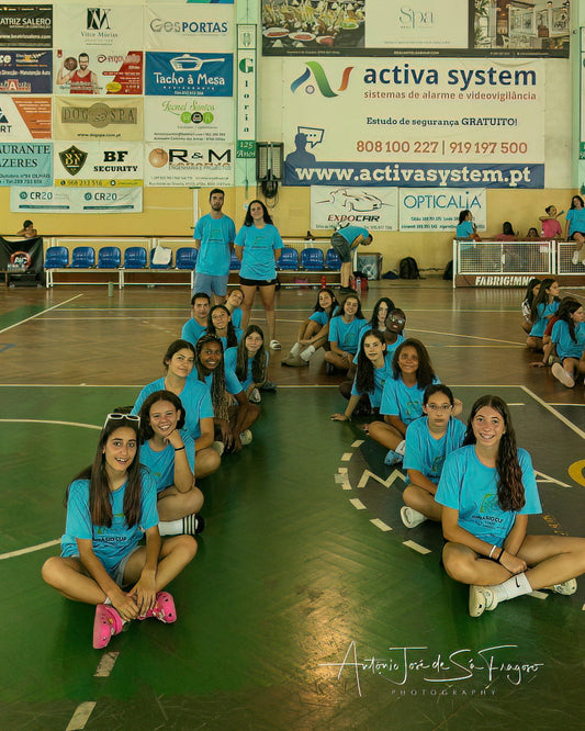 Group of people in blue shirts posing on a basketball court with various advertisements in the background.