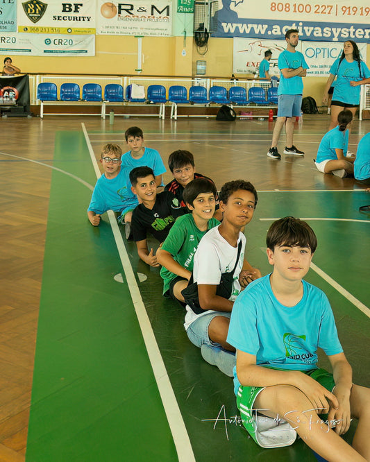 Children sitting on a basketball court with sports equipment, surrounded by gymnasium equipment and banners.