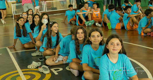 Group of children in blue shirts sitting on a basketball court.