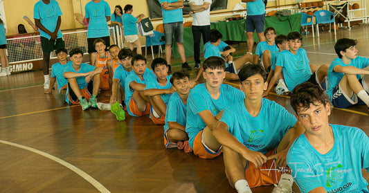Group of young basketball players in blue jerseys sitting on a basketball  court.