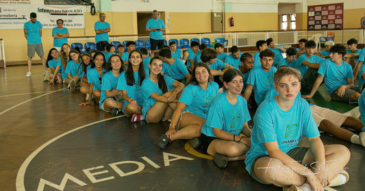 Group of people in blue shirts sitting on a gym floor with 'Media' branding.