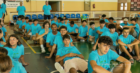 Group of people in blue shirts sitting on a gym floor.