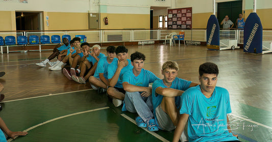 Group of young men in blue shirts sitting on a basketball court.