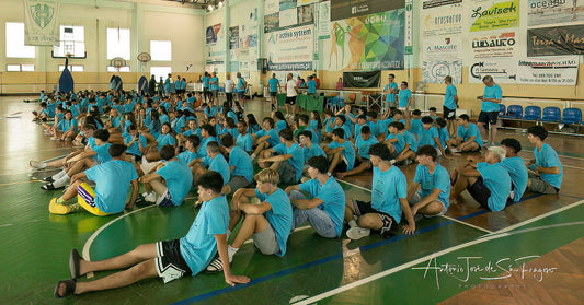 Group of people in blue shirts sitting on the floor in a gymnasium.