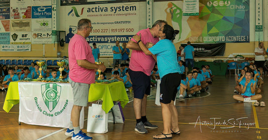 Two adults embracing on a basketball court with children and coaches in the background.