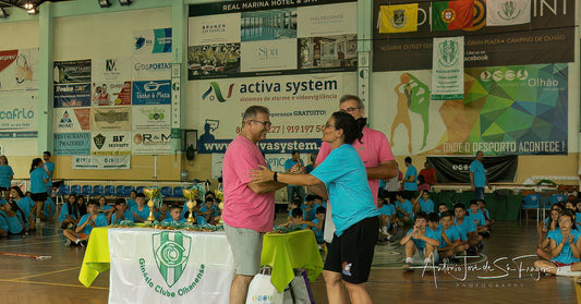 Two men shaking hands in a sports arena with banners and spectators in the background