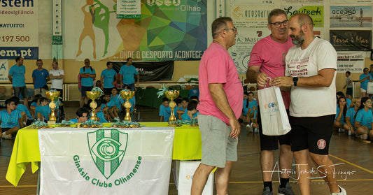 Two men standing next to a table with trophies and a banner in an indoor sports setting.