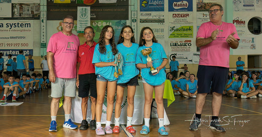 Three young women in blue sports uniforms standing on a basketball court with two men, holding trophies.