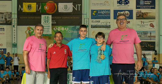 Group of people, including children in sports uniforms, standing together with a banner in the background.
