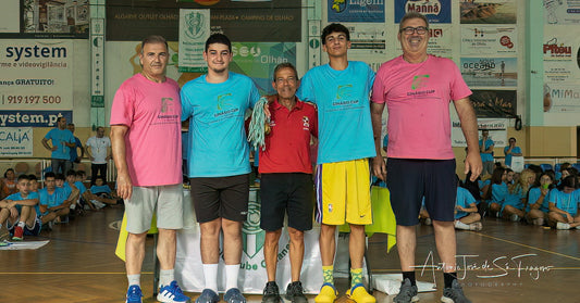 Group of people standing on a basketball court with sports equipment and spectators in the background.