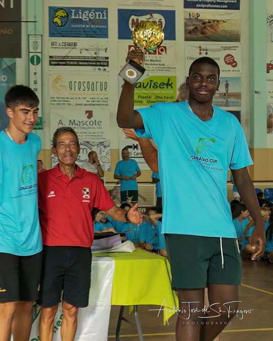 Two men in sports attire standing in a gymnasium with a banner in the background and one holding a trophy