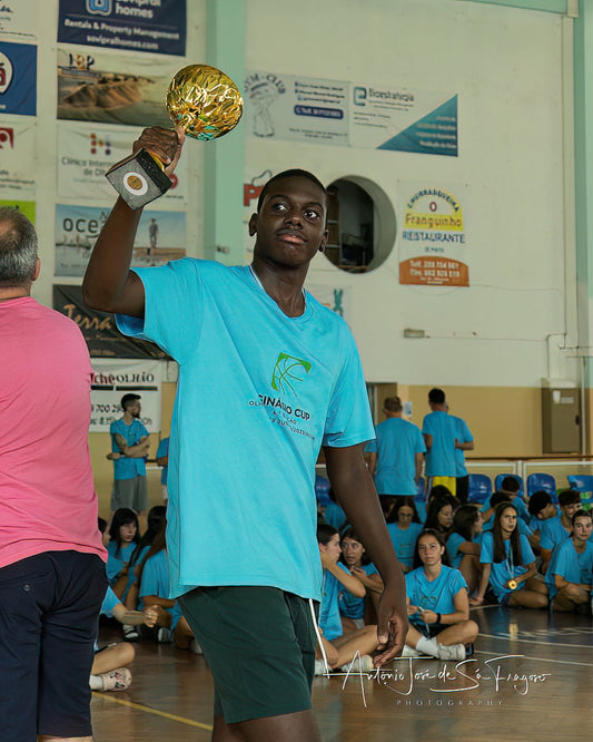 Person in a blue shirt holding a gold trophy in an indoor sports setting with spectators.