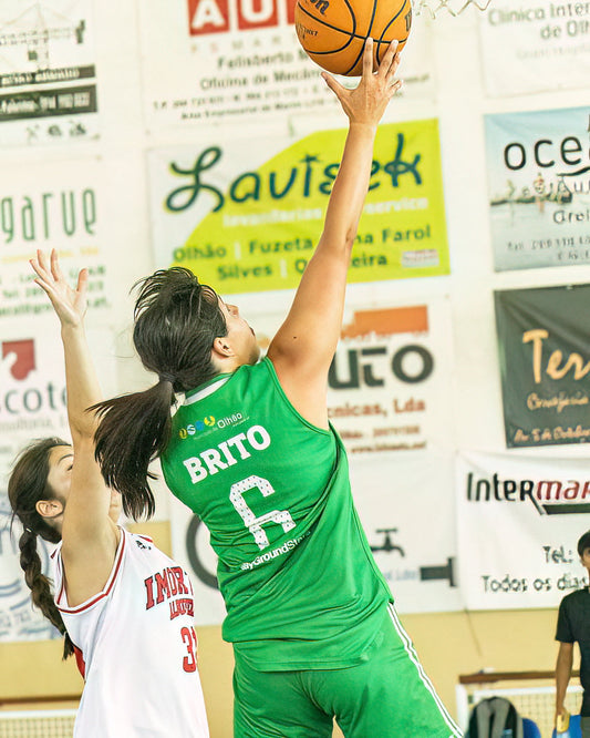 Basketball player in green jersey with 'BRITO' and number '6' attempting a shot against a defender in a gymnasium.