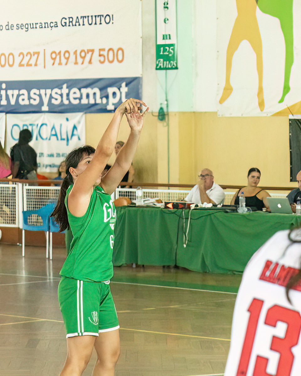 Basketball player in green uniform taking a shot during a game, with spectators and banners in the background.