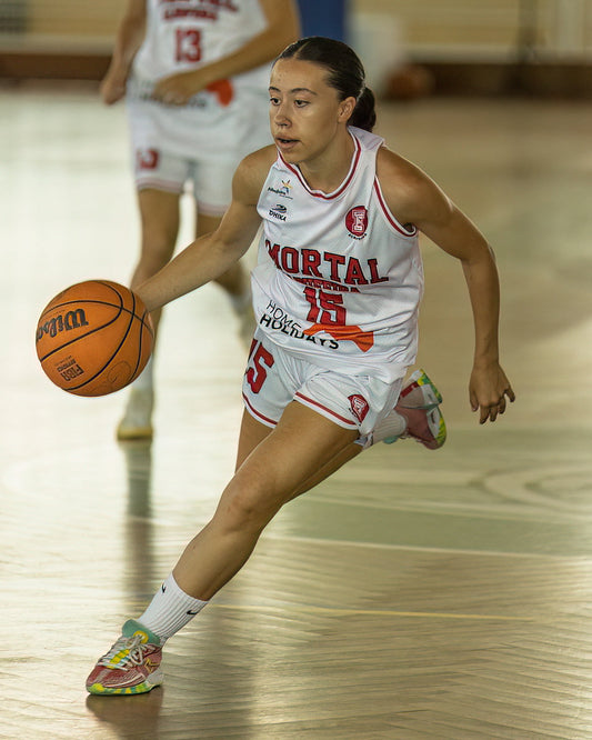 Woman playing basketball on a court with 'Mortal' branding