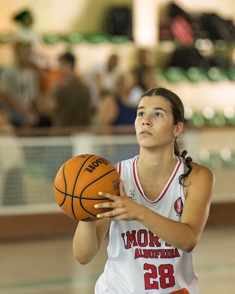 Young woman holding a basketball on a sports court with spectators in the background