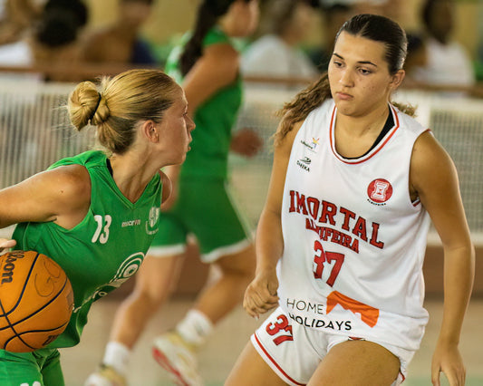 Two female basketball players in action during a game, one in a green jersey and the other in a white jersey with 'Imortal' branding.