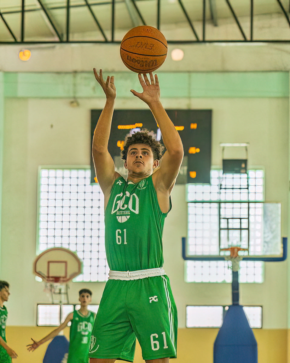 Person in green basketball uniform preparing to shoot a basketball in a gym.