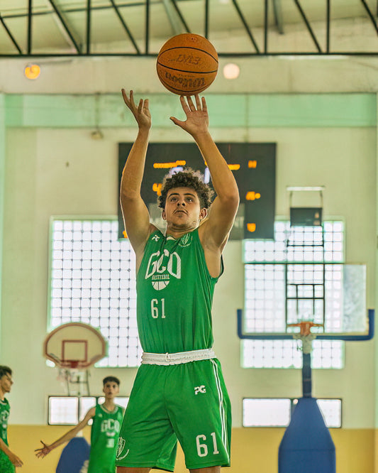 Person in green basketball uniform preparing to shoot a basketball in a gym.